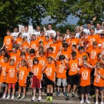 Winkende Kinder und Trainer mit orangefarbenem Wiora T-Shirt an